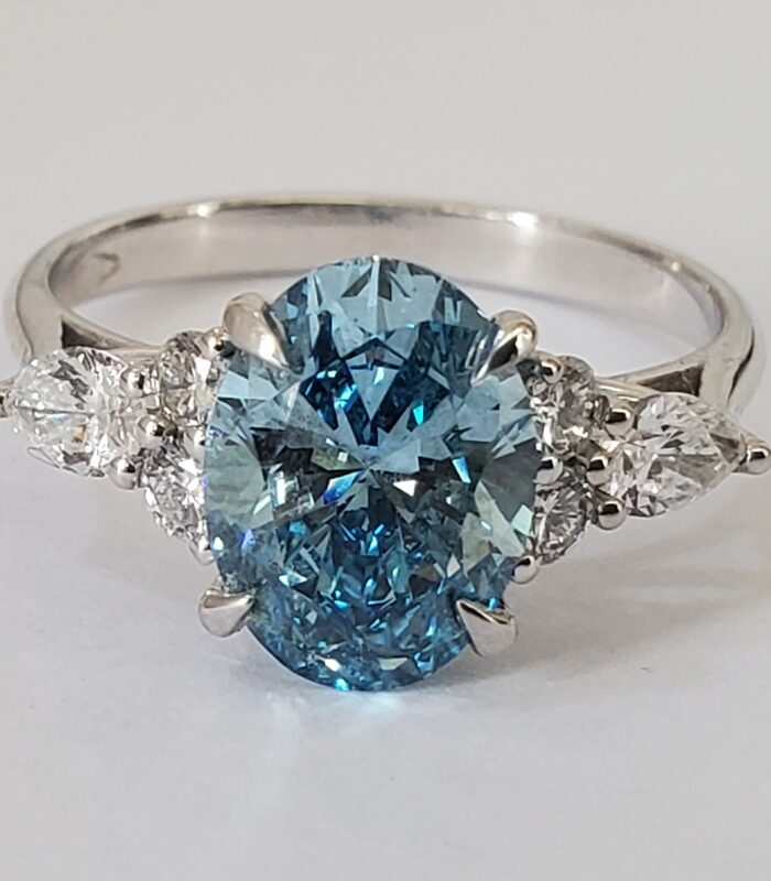 BLUE OVAL LAB DIAMOND ACCENTED WITH ROUND STONES 18KT GOLD